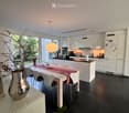 Modern kitchen with white cabinets, black countertops, a central island, a dining table with chairs, and a vase with branches on a side table.