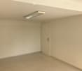Empty room with white walls, tiled floor, and a single door. A ceiling light fixture is visible.