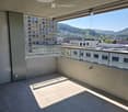 Modern balcony with tiled floor, glass railing, and a view of the city and surrounding hills.