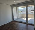 Empty room with wooden flooring, large sliding glass doors leading to a balcony with a view of the city and surrounding landscape.