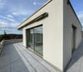 Modern balcony with tiled flooring, white walls, large glass sliding doors, and a metal railing.