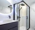 Modern bathroom with marble walls, a sleek sink, a glass-enclosed shower, and a toilet.