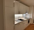 Modern kitchen with white cabinets, a sink, and an oven, featuring a wooden floor and a window with blinds.