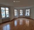 Empty room with wooden flooring and large windows, featuring radiators under the windows.