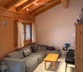 Cozy living room with exposed wooden beams, grey sectional sofa, wooden coffee table, small round table, and decorative items.