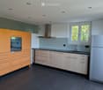 Modern kitchen with light wood cabinets, stainless steel appliances, and a black countertop.
