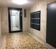 Modern hallway with beige stone walls, mosaic tile floor, black mailboxes, and a glass door leading to another area.