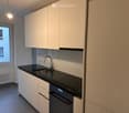 Modern kitchen with white cabinets, black countertop, stainless steel sink and faucet, and a dishwasher. Features a window with a view of the street.