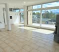 Bright, open living space with large windows and sliding doors leading to a balcony, tiled floor, fireplace, and a small screen on a stand.