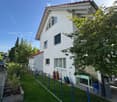 A well-maintained garden area with a neatly trimmed lawn, a wooden raised bed, potted plants, and a small patio with outdoor furniture.