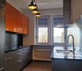 modern kitchen with orange cabinets, stainless steel sink, black countertops, white radiator, large windows with view