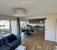Open-plan living and dining area with a grey sofa, white coffee table, dining table with green chairs, and a modern kitchen with grey cabinets and a sink.