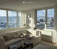 Bright living room with large windows offering a scenic view, featuring a white sectional sofa, coffee table, table lamps, and pet beds.