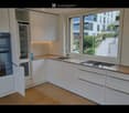 Modern kitchen with white cabinets, wooden countertops, stainless steel appliances, and large windows offering a view of the city.