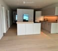 Modern kitchen with white cabinets, wooden countertops, and a central island. The floor is made of light wooden planks, and the space is well-lit with recessed lighting.