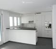 Modern kitchen with white cabinets, dark countertops, and built-in appliances, including a sink and oven. The space features large windows and a clean, minimalist design.