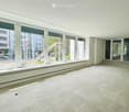 Empty room with large windows, light-colored carpeted floor, and a raised platform area near the windows.