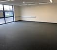 Empty room with grey carpeted floor, white walls, and large windows with blue frames. No furniture or equipment present.