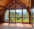 Bright, airy attic space with wooden beams, large glass doors opening to a green garden view, tiled floor, and built-in wooden shelving unit.