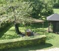 A well-maintained garden with a wooden pergola, a small wooden shed, a neatly trimmed hedge, and several potted plants.