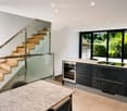 Modern open-plan space with a staircase leading to an upper level, a kitchen area with dark cabinets and stainless steel appliances, and a dining table with chairs.