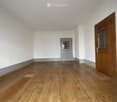 Empty room with wooden flooring, white walls, and two doors (one wooden and one grey).