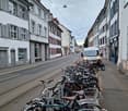 A row of classic European buildings lines a narrow street, with bicycles parked along the sidewalk and a tram passing by.