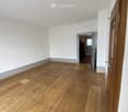 Empty room with wooden flooring and white walls, featuring a doorway leading to another room.