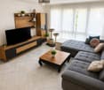 Modern living room with a grey sectional sofa, wooden coffee table, TV stand, cat tree, shelves, and potted plants.
