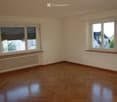 Empty room with wooden flooring, white walls, large windows with blinds, and radiators beneath the windows.
