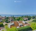 Aerial view of a suburban neighborhood with multiple houses, green lawns, and a scenic lake and mountain view in the background.
