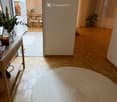 entryway with wooden floor, round woven rug, wall-mounted mirror, table with vase, shoe rack, doorway leading to kitchen
