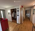 hardwood floor, white walls, large open doorway, clothes hanging, wooden dresser, framed pictures, open closet with clothes and boxes, cabinet with drawers