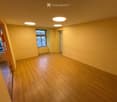 Empty room with wooden flooring, light yellow walls, and recessed ceiling lights. There are windows and a doorway leading to another space.