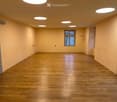 Empty room with wooden flooring, light-colored walls, and recessed ceiling lights. A single window provides natural light.