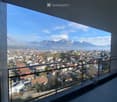 Balcony with a modern glass railing, overlooking a town with houses and distant snow-capped mountains.