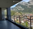 Modern balcony with a metal railing, overlooking a town and mountain landscape.