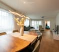 large windows, white walls, modern chandelier, wooden floor, modern furniture, dining table, chairs, living room, couch, center table, TV, pictures