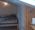 Cozy attic bedroom with wooden floors, slanted ceilings, and a skylight. Features a small bed with pillows and blankets, a wooden table with a chair, and a picture frame on the wall.