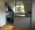 Modern kitchen with wooden flooring, stainless steel appliances, and a large window overlooking a green area.