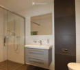 Bathroom. Modern bathroom with a white sink, mirror, toilet, and glass-enclosed shower. The sink has a sleek faucet and a small cabinet with brass handles. The shower features a modern handle and a glass door.