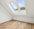 Empty attic room with wooden floors, white walls, and two large skylights with views
