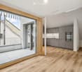 Modern, open-plan space with a balcony area and a kitchen. Features include wooden flooring, grey kitchen cabinets, a built-in oven, and a large sliding glass door leading to a tiled balcony.