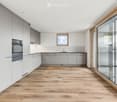 empty kitchen with wooden floor, glass sliding doors, white cupboards, window, modern design