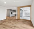 Empty room with wooden floor, white walls, large windows, and a view of another room.