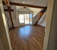 Empty attic space with wooden flooring, exposed wooden beams, and a door leading to a balcony.