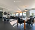 Modern dining and living area with dark tiled flooring, large windows, a dining table with chairs, a sofa, coffee table, and decorative items.