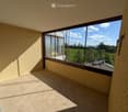 Empty balcony with tiled floor, large windows offering a view of a green landscape and distant buildings.