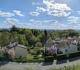 A scenic view of a residential area with houses, trees, and a clear blue sky, featuring a distant landscape and rolling hills.