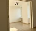 Empty room with beige tiled floor, white walls, and a small window letting in natural light. The room has a modern ceiling light fixture and a radiator near the window.